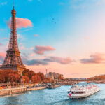 The main attraction of Paris and all of Europe is the Eiffel tower in the rays of the setting sun on the bank of Seine river with cruise tourist ships